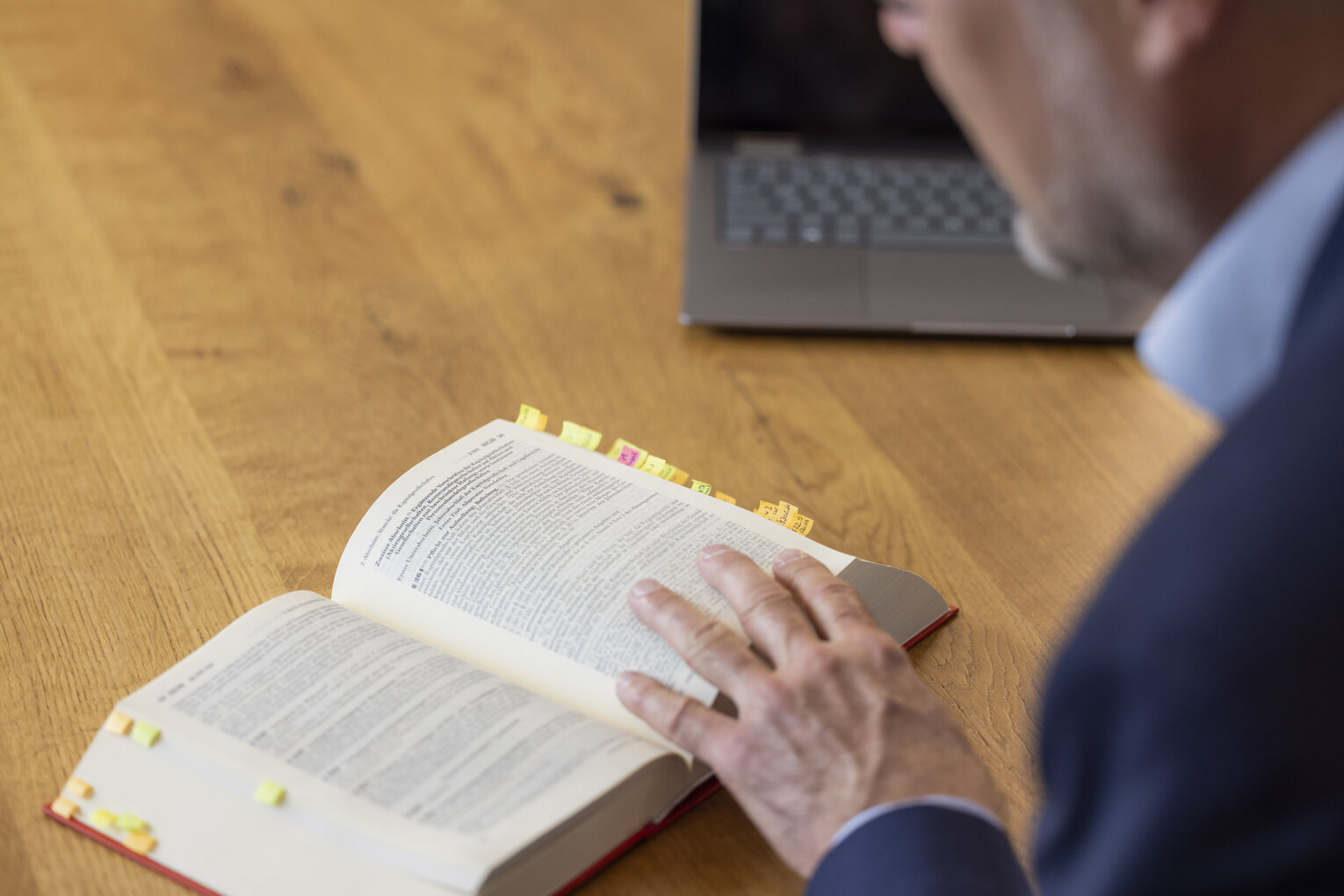 Gesetzesrecherche Mann blättert in einem aufgeschlagenen Gesetzbuch mit Markierungen.